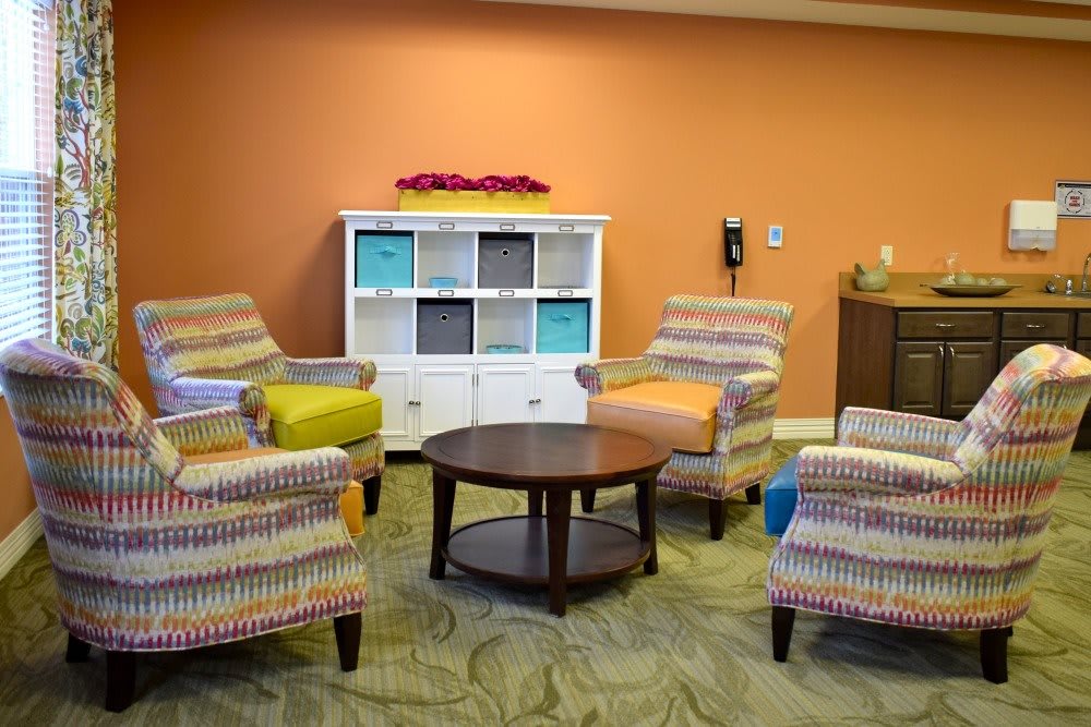 A cozy living room with striped armchairs and a round coffee table in front of an orange wall.