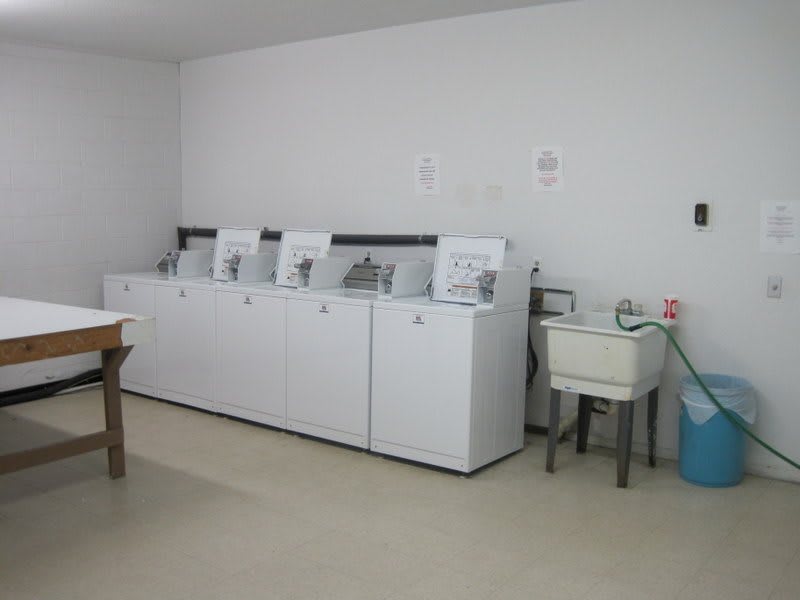 A laundry room with several washing machines lined up next to a sink.