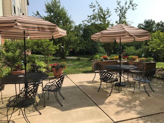 A sunny patio area with tables, chairs, and umbrellas surrounded by lush greenery.