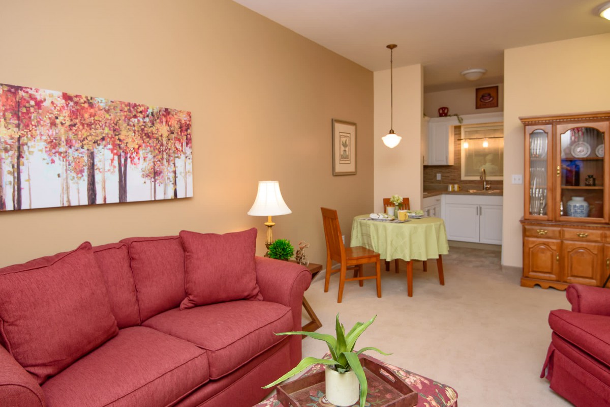 A cozy living and dining area with a red sofa, decorative wall art, and a small kitchen in the background.