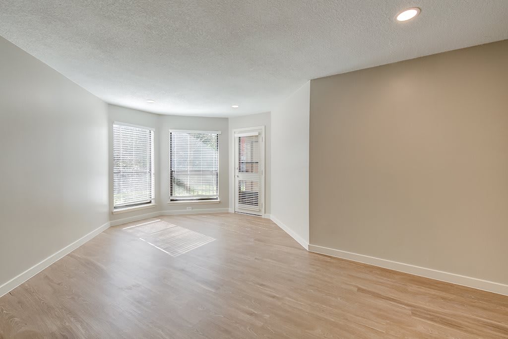 A bright, empty room with large windows and hardwood flooring.