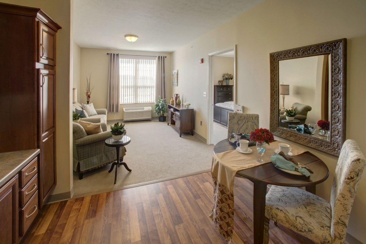 A cozy, well-lit living room with a mix of wooden flooring and carpet, featuring comfortable furniture and tasteful decor.