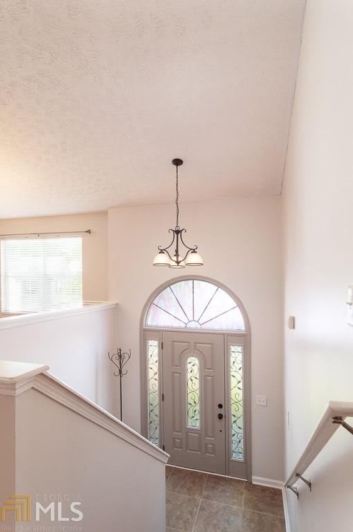 A bright interior entrance with a staircase, chandelier, and arched window above the front door.