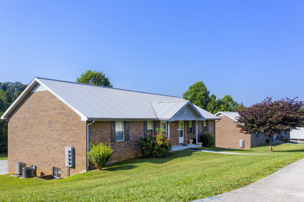 A single-story brick house with a sloping lawn and clear blue sky.