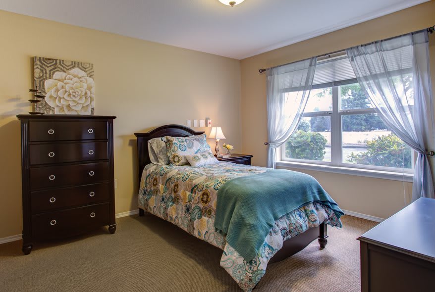 A cozy bedroom with a single bed, dresser, and large window.