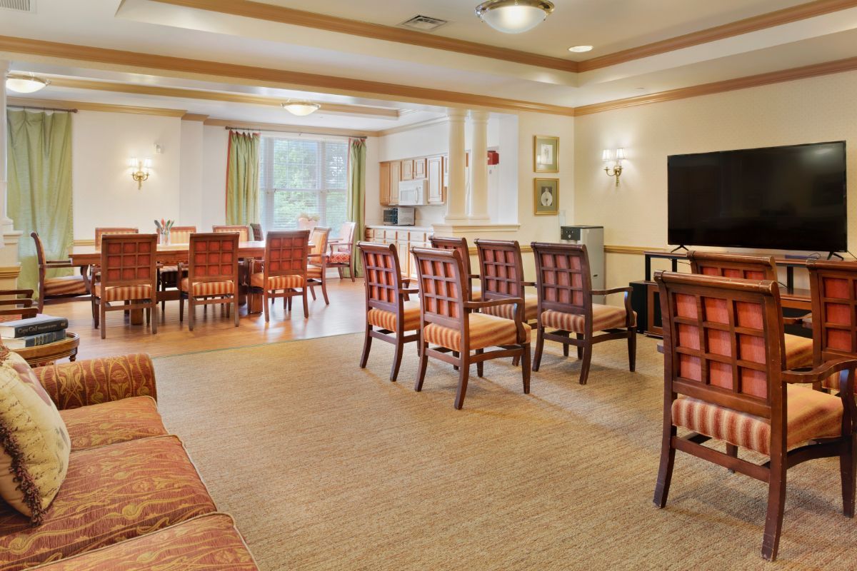 A spacious dining room with multiple tables and chairs arranged neatly, featuring comfortable seating and natural light from large windows.