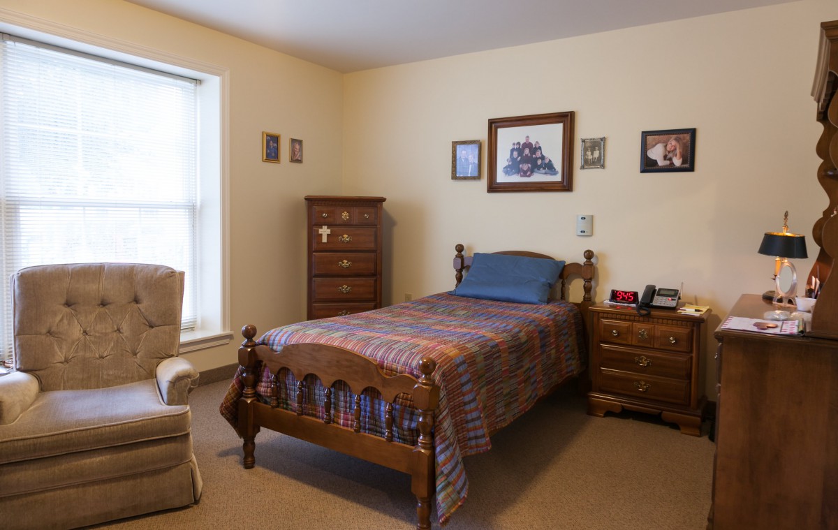 A cozy bedroom with a single wooden bed, dresser, and upholstered chair.