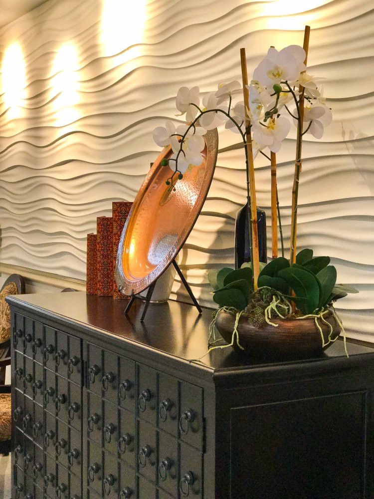An elegant interior setup with a modern wavy wall design, featuring an orchid arrangement and decorative items on a dark wooden table.