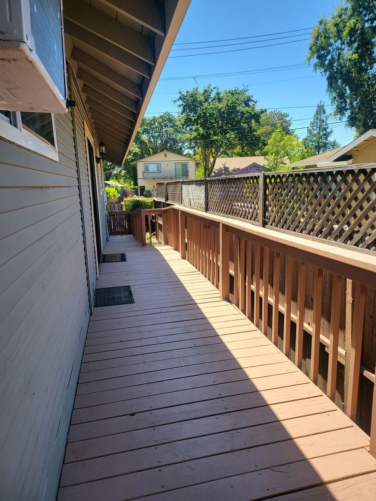 A sunny view of a wooden deck alongside a house with a fence.