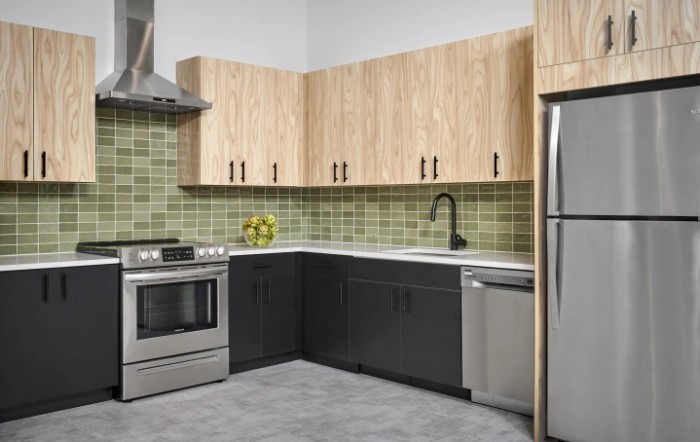 A modern kitchen featuring stainless steel appliances, wooden cabinets, and a green tile backsplash.