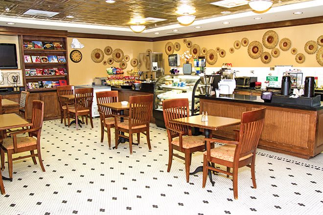 A cozy cafe interior with wooden tables and chairs, decorative plates on the wall, and a counter with coffee machines.