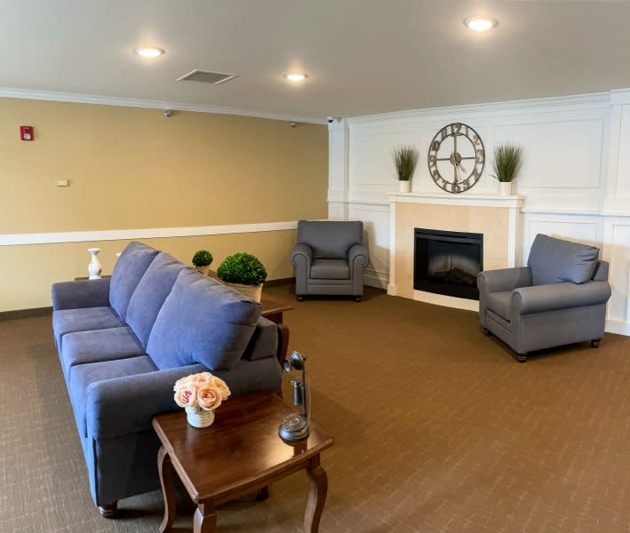 A cozy living room featuring a blue sofa and armchairs, a wooden coffee table with floral decor, and a fireplace adorned with a large clock.