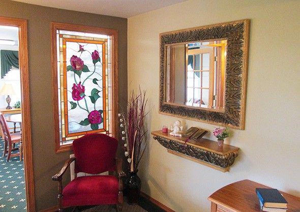 A cozy interior corner with a stained glass window, ornate mirror, and elegant red chair.