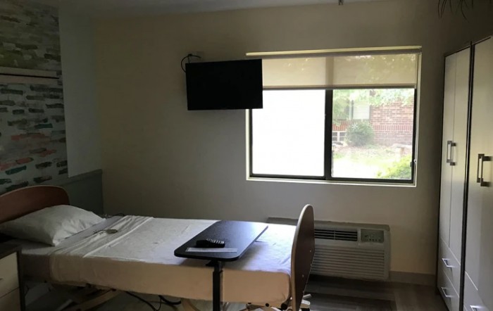 A hospital room with a bed, tray table, and television.