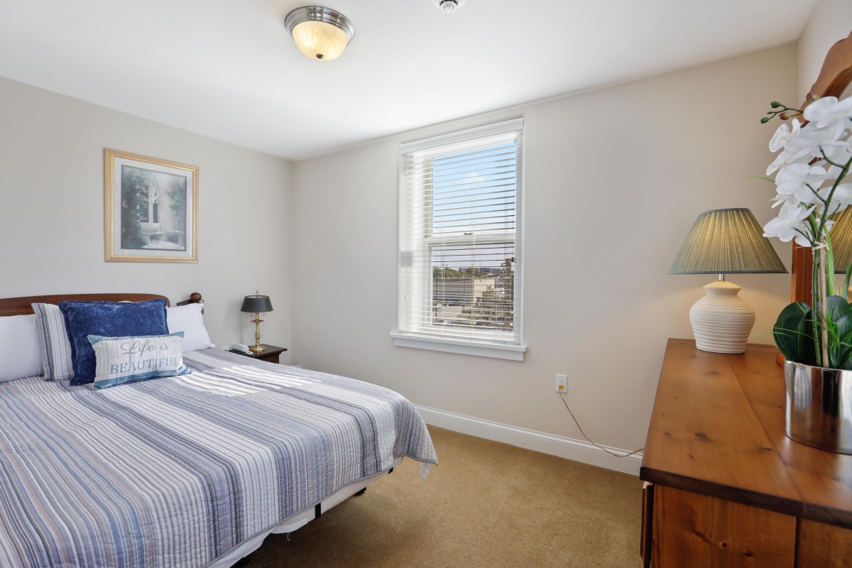 A tidy bedroom with a bed, dresser, and window with blinds.