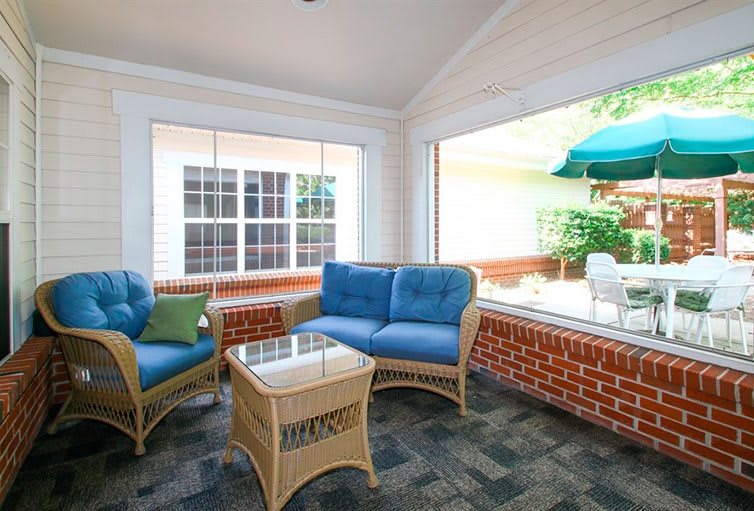 A cozy sunroom with wicker furniture and blue cushions overlooks a bright patio area.