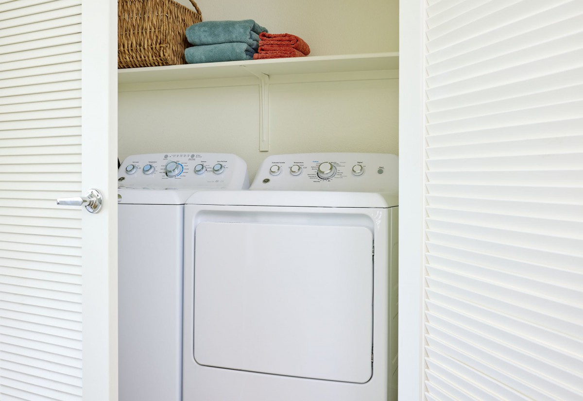 A small laundry room with a washing machine and dryer, featuring shelves with folded towels.