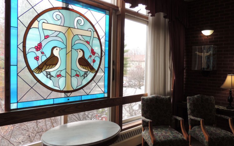 A cozy room featuring a colorful stained glass window with bird designs, and comfortable seating.