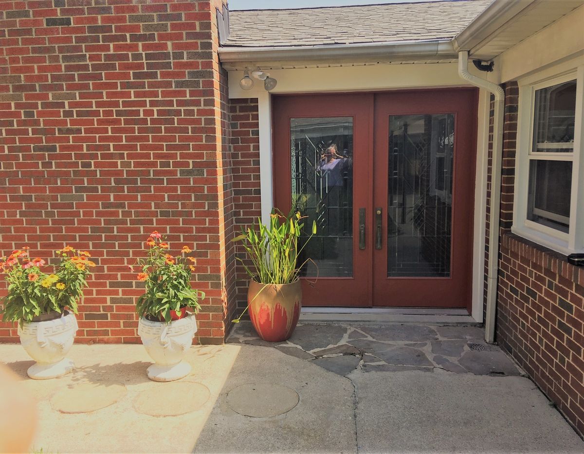 A house entrance featuring a brick wall, glass double doors, and potted plants.