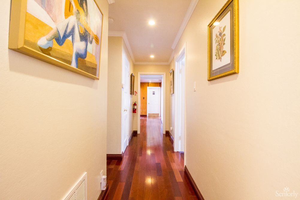 A brightly lit hallway with wooden floors and decorative paintings on the walls.