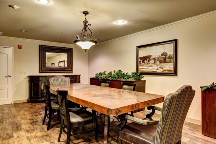 A cozy dining room with a large wooden table surrounded by chairs, featuring a chandelier and decorative elements like a painting and a mirror.