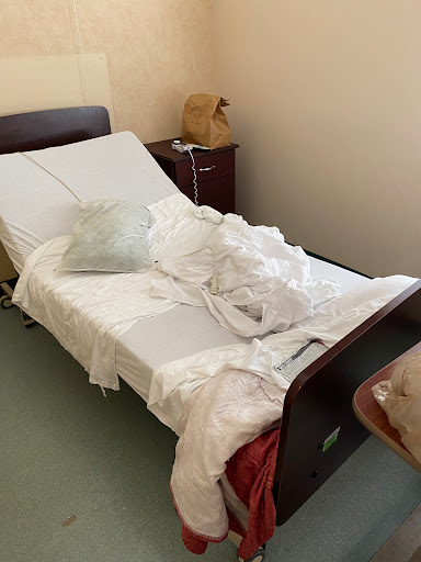 A disheveled hospital bed with crumpled linen in a care room.