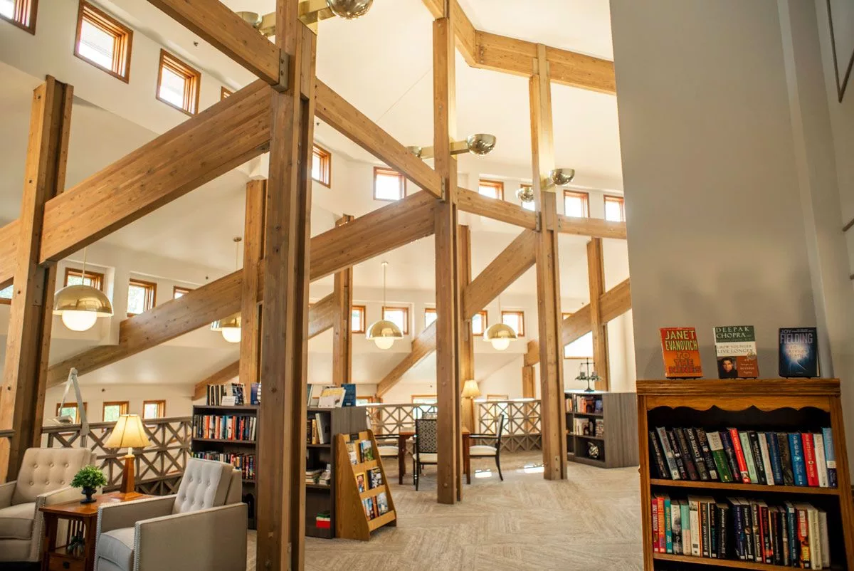 A cozy library interior with wooden beams and ample natural light filtering in through large windows.