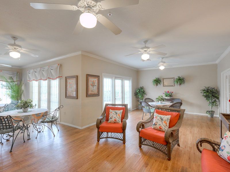 A bright and spacious living room featuring orange-accented chairs, wood flooring, and a dining area in the background.