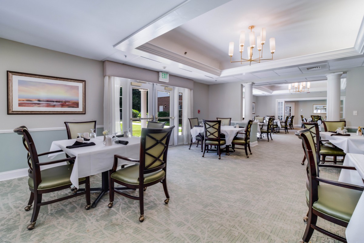 An elegant dining room with neatly arranged tables and chairs, illuminated by natural light and a chandelier.