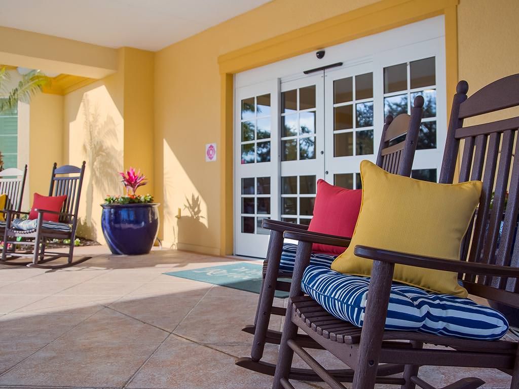 A cozy patio setting with a rocking chair and colorful cushions in front of an entrance with glass doors.