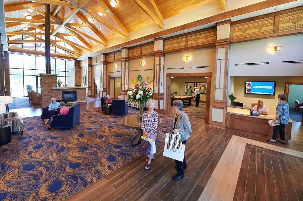 A spacious lobby with wooden ceilings, comfortable seating, and two people walking with shopping bags.