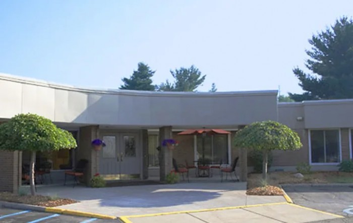 A modern building with a patio area, featuring outdoor seating and surrounded by trees on a sunny day.