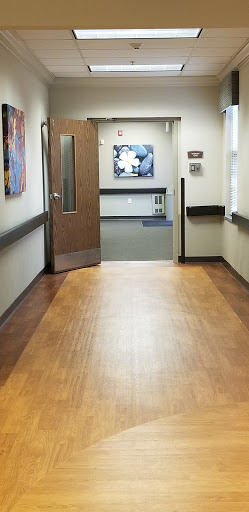 A tranquil hospital hallway showcasing wooden flooring and artwork on the walls.