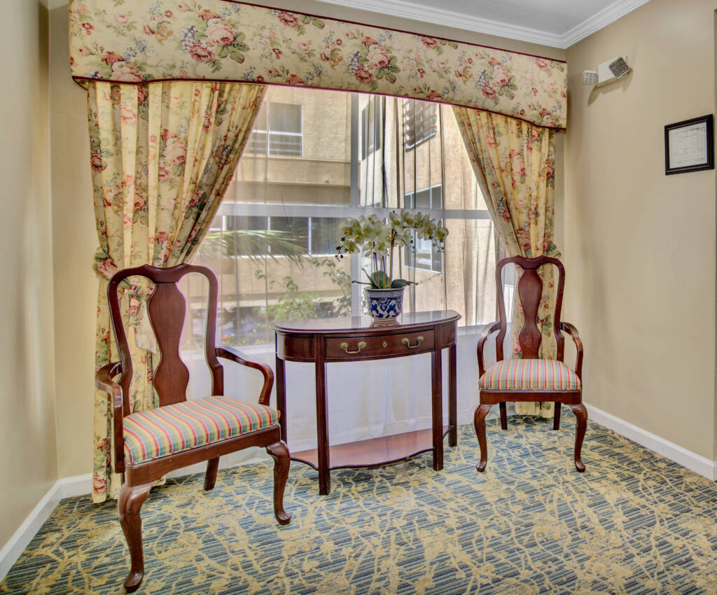 A traditional room interior with two wooden chairs, a small table, and floral curtains.