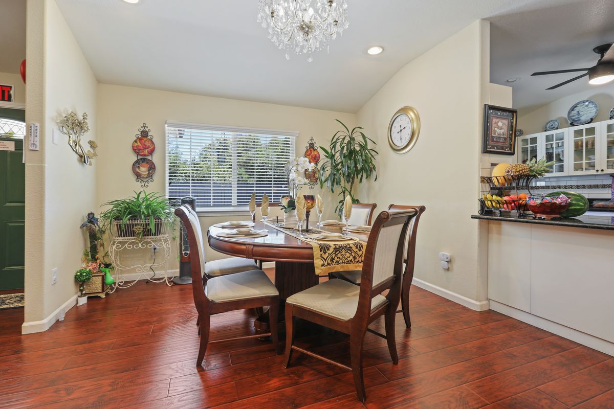 A cozy dining room with a wooden table and chairs, illuminated by a chandelier and decorated with plants and wall art.
