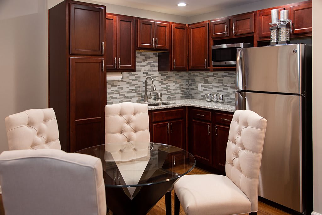 A modern kitchen and dining area with wooden cabinets, stainless steel appliances, and upholstered chairs.