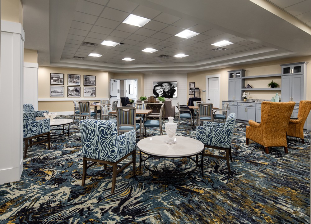 A modern lobby featuring a seating area with patterned chairs, round tables, and decorative elements on a carpeted floor.