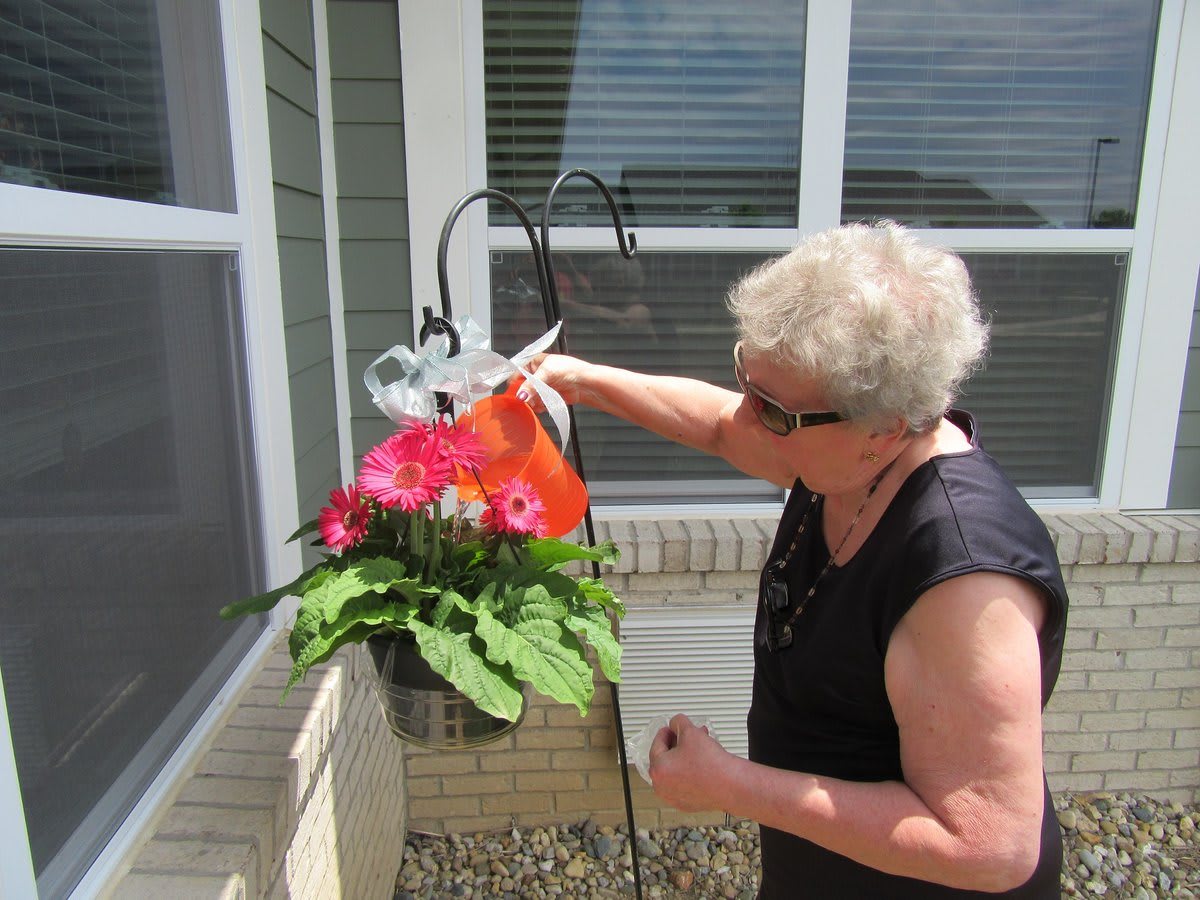 A senior woman waters flowers in a hanging pot outdoors.
