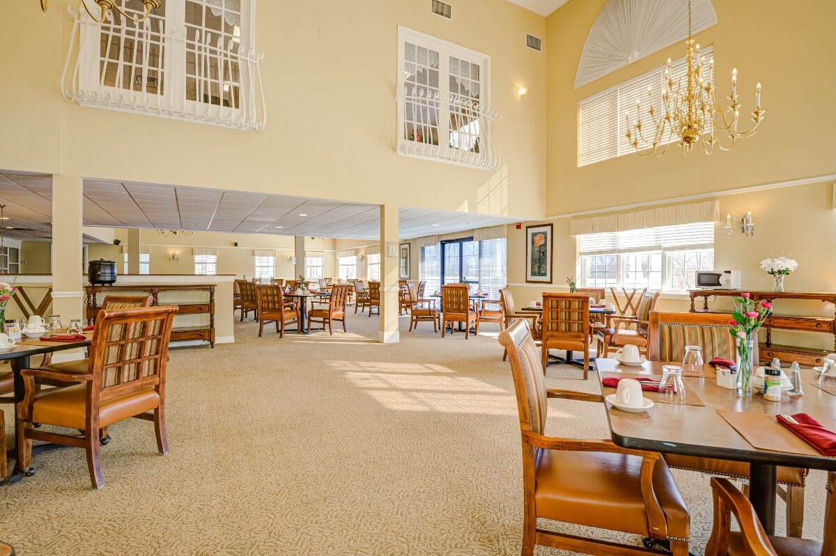 A spacious and brightly lit dining area with wooden chairs and tables, featuring large windows.