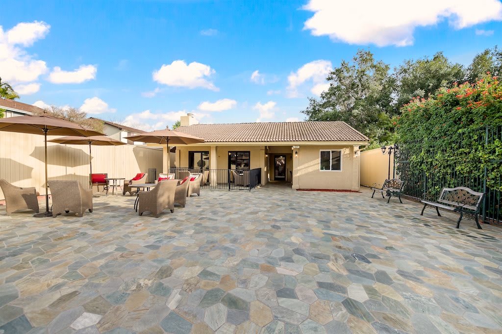 A spacious backyard with a tiled patio and outdoor furniture under a bright blue sky.