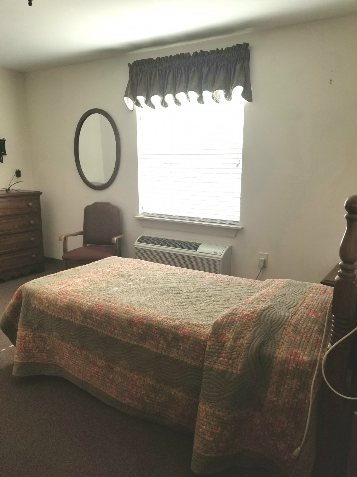 A cozy bedroom with a bed, dresser, chair, and window.