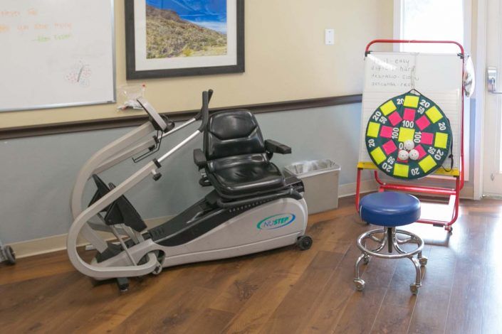 A therapy room with a recumbent exercise bike and a colorful spinner wheel for exercises or games.