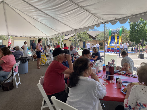 A lively outdoor gathering under a tent, filled with families enjoying food and festivities.