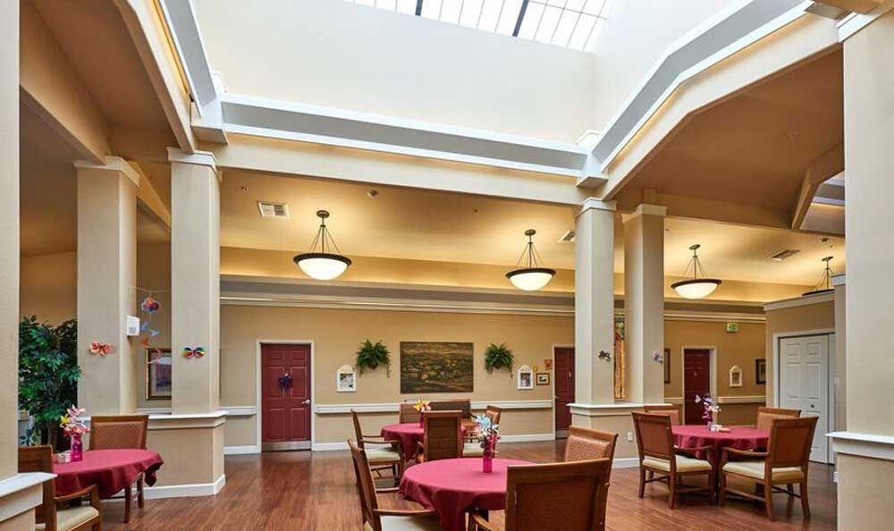 A well-lit dining area with round tables and chairs, featuring a skylight and elegant columns.