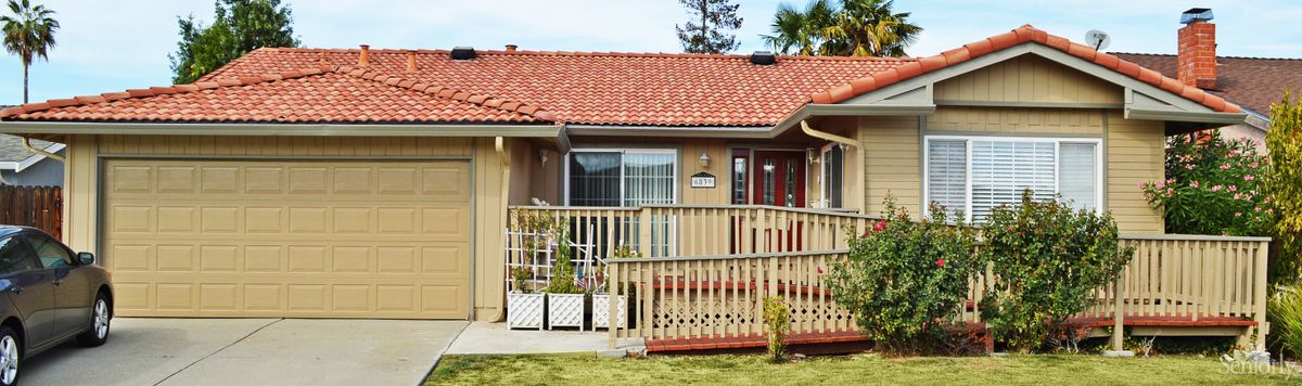A quaint house with a red-tiled roof and wooden deck surrounded by a neatly kept front yard.