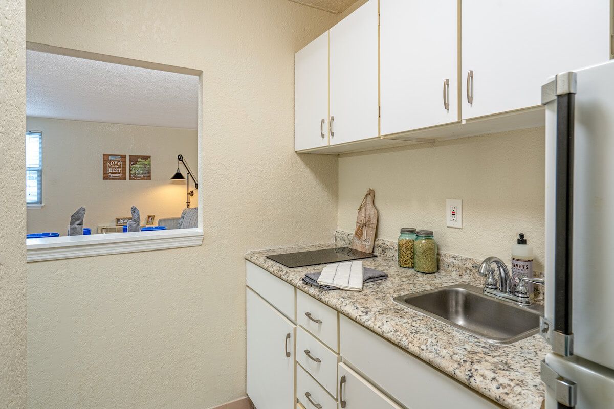 A compact kitchen with white cabinets and a granite countertop, featuring a double sink.