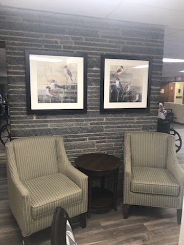 A cozy seating area featuring two striped chairs, a small table, and framed artwork on a stone wall.