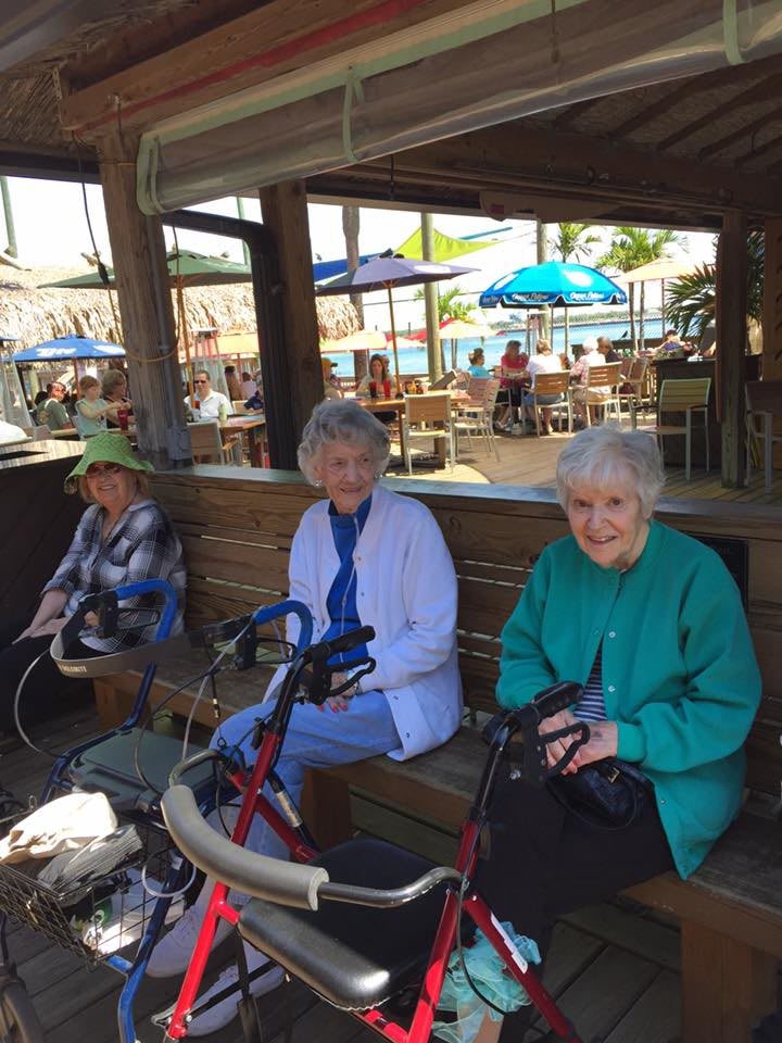 Three elderly individuals sitting together outdoors under a shaded area.