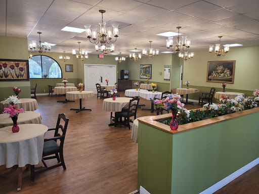 A spacious and elegantly designed dining area featuring multiple tables and chairs, adorned with chandeliers and green accents.