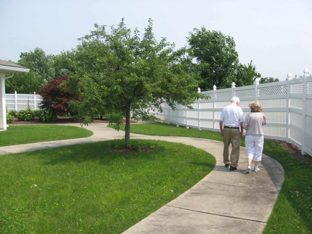 An elderly couple walking together on a pathway in a park surrounded by greenery and trees.